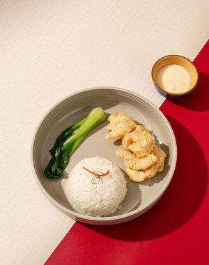 Un kızartılmış karides üzerine mayonez sosu serpilmiş ve sıcak pirinçle servis edilmiş.