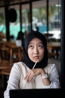 Kafede oturan tesettürlü Endonezyalı kadın. İş kadını, kafeteryadan düşünce tarzıyla çalışıyor.