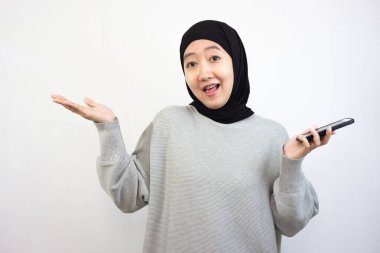 Genç gülümseyen Asyalı Müslüman kadın cep telefonu tutuyor ve neşeli bir jest yapıyor. beyaz arkaplanda izole