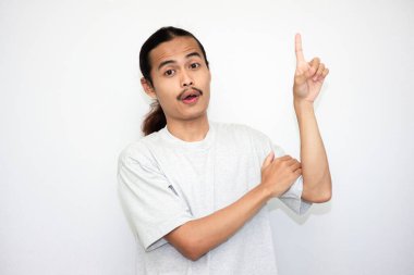 Yukarı bakan gri tişörtlü bir Asyalı. Beyaz stüdyo arka planında izole edilmiş. Uzun saçlı Asyalı adam.