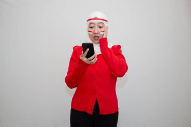 Beyaz tesettürlü, kırmızı kazaklı bir kadın. Endonezya 'nın bağımsızlık gününü kutluyoruz. Telefonu tut. Beyaz arkaplanda izolasyon.