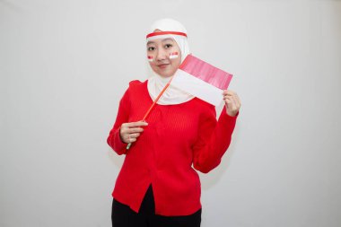 Beyaz tesettürlü, kırmızı kazaklı bir kadın. Endonezya 'nın bağımsızlık gününü kutluyoruz. Bayrağı heyecanla tutuyor. Beyaz arkaplanda izolasyon.