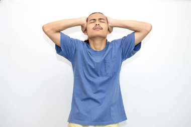 Baş ağrısından muzdarip koyu mavi t-shirt giyen Asyalı genç adam, acıdan yüz ifadesiyle kurtulmak için el alna bastırıyor.