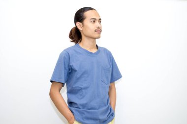 Koyu mavi tişört giyen gülümseyen Asyalı adam elleri ceplerinde duruyor. beyaz arkaplanda izole