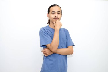 Koyu mavi tişört giyen gülümseyen Asyalı adam elleri çenesinde duruyor. beyaz arkaplanda izole