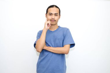 Koyu mavi tişört giyen gülümseyen Asyalı adam, elini yanağına değdirip öne bakıyor. beyaz arkaplanda izole