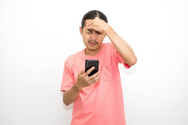 Pembe t-shirt giyen Endonezyalı, Asyalı bir adam baş ağrısı çekiyor ve elinde telefonla elini tutuyor. beyaz arkaplanda izole