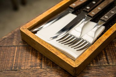 A wooden holder with cutlery, including a knife, fork, and napkin, arranged neatly. This setup gives a rustic and elegant dining atmosphere, ideal for table settings clipart