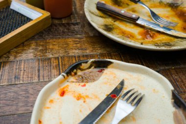 A cream-colored plate with a beautiful pattern shows leftover food, including a knife and fork. Some sauce remains on the plate, indicating the end of a meal clipart