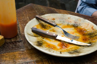 A cream-colored plate with a beautiful pattern shows leftover food, including a knife and fork. Some sauce remains on the plate, indicating the end of a meal clipart