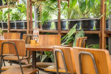 Ahşap sandalyeli bir restoranın ve çömleklere yeşil bitkiler ekilmiş masaların ortamı.