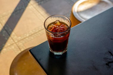 Buzlu bir amerikan kahvecinin masasında servis edildi. Arka planda da da rahat bir kafe ortamı vardı. Soğuk içecek, kafe ortamının rahatlatıcı atmosferine katkı sağlıyor.