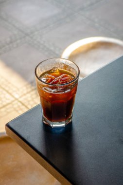 Buzlu bir amerikan kahvecinin masasında servis edildi. Arka planda da da rahat bir kafe ortamı vardı. Soğuk içecek, kafe ortamının rahatlatıcı atmosferine katkı sağlıyor.