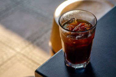 Buzlu bir amerikan kahvecinin masasında servis edildi. Arka planda da da rahat bir kafe ortamı vardı. Soğuk içecek, kafe ortamının rahatlatıcı atmosferine katkı sağlıyor.