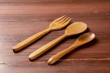 Tahta bir arka plana yerleştirilmiş izole edilmiş bir tahta kaşık ve çatal doğal dokularını ve tasarımlarını sergiliyor. Sahnenin basitliği kırsal zarafeti vurguluyor.