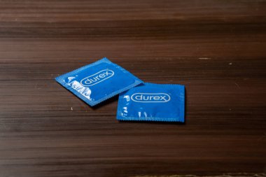 Ahşap bir masaya yerleştirilmiş, basit ambalaj tasarımını gösteren Durex mavisi bir prezervatif kutusu. Doğal ahşap dokusu sahnelere kırsal bir dokunuş katıyor.