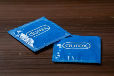 Ahşap bir masaya yerleştirilmiş, basit ambalaj tasarımını gösteren Durex mavisi bir prezervatif kutusu. Doğal ahşap dokusu sahnelere kırsal bir dokunuş katıyor.