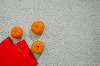 Çin kutlamalarında refahı, iyi talihi ve mutluluğu simgeleyen beyaz bir arka planda izole edilmiş kırmızı angpao ve mandalina portakalları.