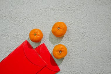 Çin kutlamalarında refahı, iyi talihi ve mutluluğu simgeleyen beyaz bir arka planda izole edilmiş kırmızı angpao ve mandalina portakalları.