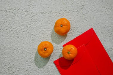 Çin kutlamalarında refahı, iyi talihi ve mutluluğu simgeleyen beyaz bir arka planda izole edilmiş kırmızı angpao ve mandalina portakalları.