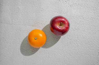 Temiz beyaz bir zemin üzerinde izole edilmiş koyu kırmızı bir elma ve portakal. Sağlığı, tazeliği ve doğal iyiliği sembolize ediyor. Yiyeceklerle ilgili görseller için mükemmel.