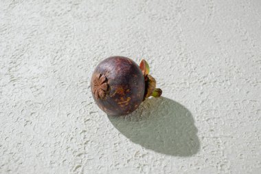 Mangosteen meyvesi, eşsiz mor kabuğunu ve tazeliğini vurgulayarak, desenli beyaz arka planda sergilenir.