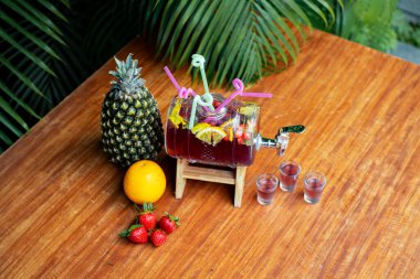 A Refreshing Sangria Cocktail With Colorful Garnishes, Served In A Unique Container On A Wooden Table, Surrounded By Lush Green Leaves, Offering A Natural Vibe on Top. clipart