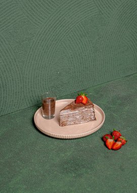 Çilek soslu bir dilim çikolatalı pasta ve kahverengi yuvarlak bir tabakta zarif bir şekilde servis edilen çikolata sosu..