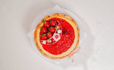 Çilekli kek, taze çilek soslu, bayan parmaklarıyla süslenmiş, ve pembe saten kurdeleli, beyaz pasta standında servis edilmiş,.