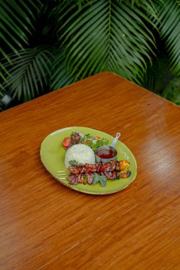 Buharda pişmiş pirinçli ızgara barbekü bifteği, taze salata ve ahşap masadaki yeşil tabakta lezzetli sos..