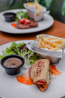 Sığır eti, erimiş peynir, patates kızartması, taze salata ve beyaz tabakta mantar sosu ve bir biftek daha..