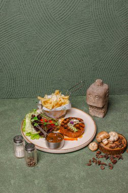 Biftek, patates kızartması, taze salata ve beyaz tabakta mantar sosuyla servis ediliyor..