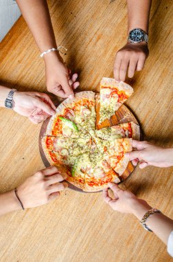 Elleri, ahşap bir masadan pizza dilimini alıyor lezzetli ve lezzetli bir yemeğin tadını çıkarmaya hazır..