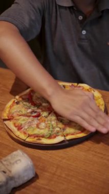 Pizza masanın üstünde ve pizzayı en üstte el ile kesiyor.