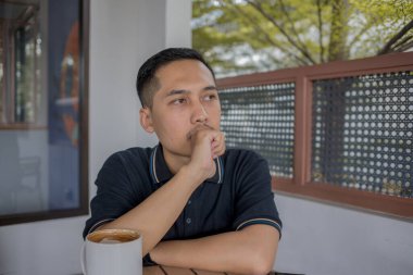 Masanın üzerinde oturmuş, bir fincan kahveyle sakin ve rahat bir ortamda düşüncelere dalmış bir adam..