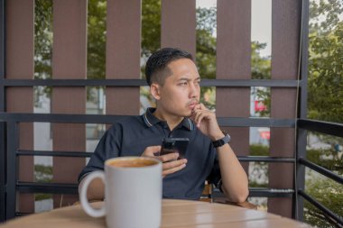 Masanın üzerinde oturup kahve içerken oturup düşünen sakin bir anda düşünceli bir ifadeyle yan tarafa bakan bir adam..