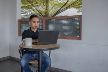 Laptopta çalışan bir adam, sıcak bir kafe atmosferindeki masada bir bardak kahveyle....