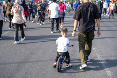 Arkasından yürüyen bir adamla bisiklete binen genç çocuk.