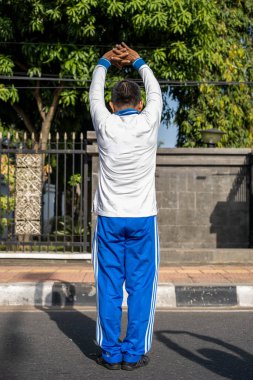 Kollarını başının üstüne geren adam, geriye doğru bakıyor.