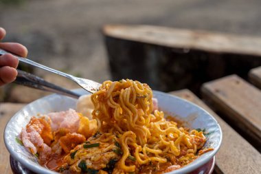 Bir kaseden çatal kaldıran baharatlı erişte.