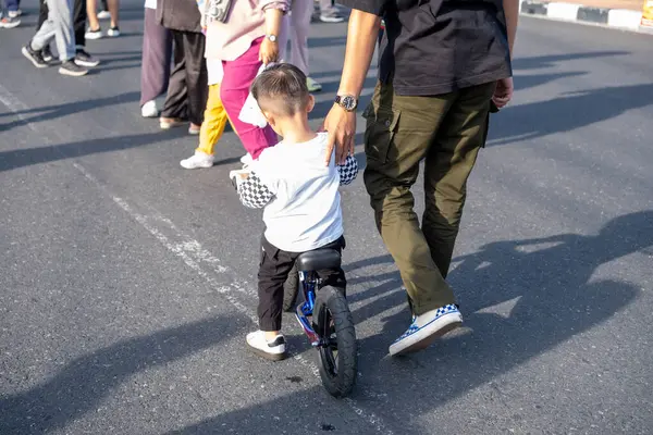 Genç bir çocuk bir adam tarafından yönlendirilirken küçük bir bisiklet sürüyor.