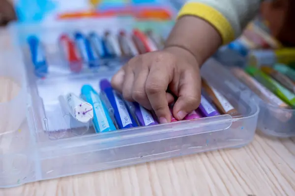 Bir çocuğun eli açık bir plastik boya kutusuna uzanır.