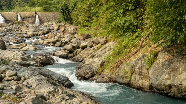 Ormandaki kayaların üzerinden akan baraj, arkaplanda beton baraj olan ormandaki kayaların üzerinden akan Turkuaz nehri.