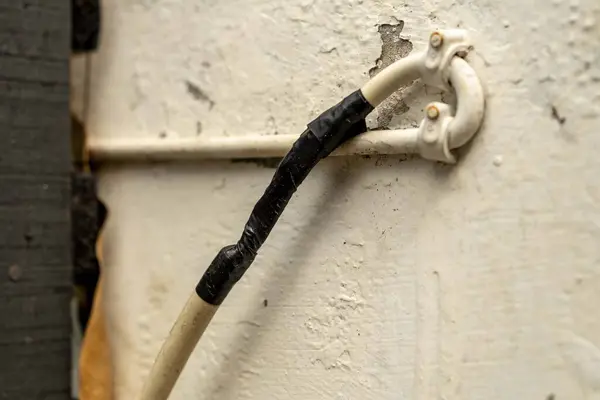 Hasarlı elektrik kablosu beyaz bir duvardaki yalıtım bandıyla onarılıyor.
