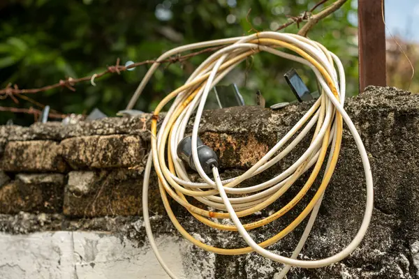 Eski elektrik kablosu, üzerinde dikenli teller olan taştan bir duvara asılmış, güvenlik ve güvenlik eksikliğini gösteriyor.