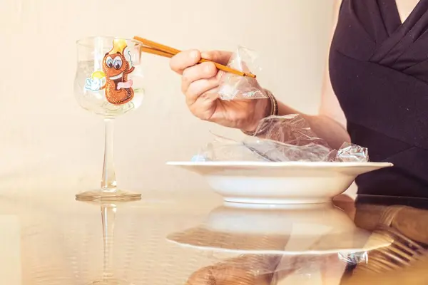 Şık bir gece elbisesi giymiş bir kadın öğle yemeğinde oturur. Yemek çubuklarıyla plastik yiyor..