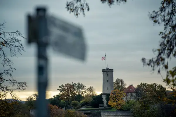 Ön plandaki bulanık tabela arka plandaki Bielefeld Sparrenburg 'u işaret ediyor. Çok bulutlu, ama ufuktaki altın renkli güneş şeridi güneşin yeni doğduğunu gösteriyor..