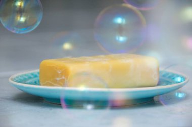 Turkuaz bir plaka üzerinde sarı sabun, etrafında sabun köpükleri yüzer.