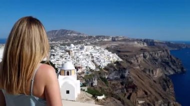 Sarı saçlı bir kadın, Yunanistan 'ın Santorini kentindeki beyaz ev ve denizin panoramik manzarasının keyfini çıkarıyor