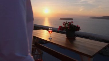 Deniz kenarında güzel bir gün batımında şarap içen bir kadın etrafındaki huzurlu manzarayı yansıtır.